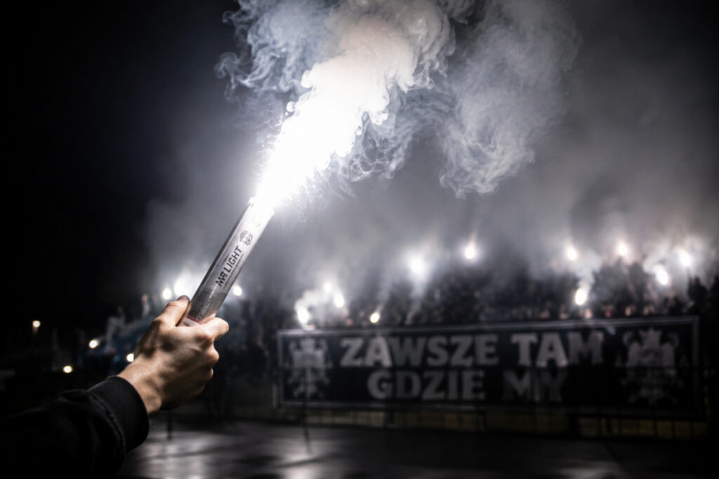 Biała flara stadionowa trzymana w dłoni podczas oprawy kibicowskiej ultras na trybunach