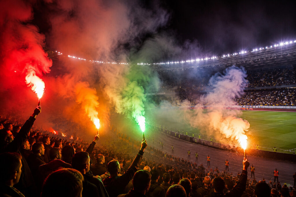 Kolorowe flary stadionowe emitujące czerwone zielone i pomarańczowe światło podczas nocnego wydarzenia sportowego