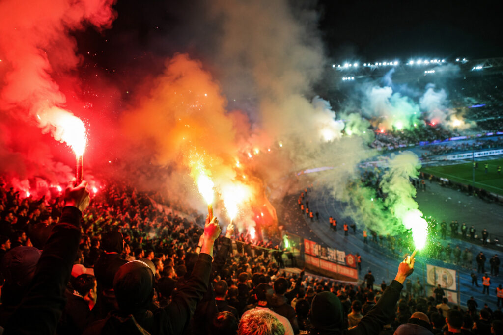 Kolorowe flary stadionowe emitujące czerwone zielone i pomarańczowe światło podczas nocnej oprawy na stadionie