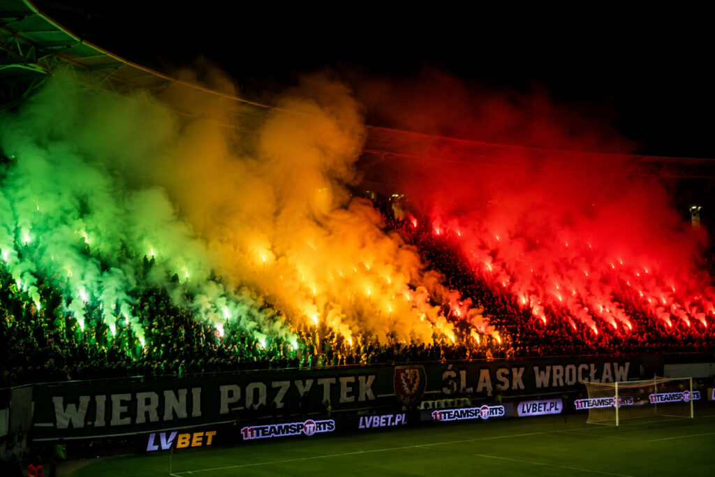 Kolorowe flary stadionowe w kolorze zielonym żółtym i czerwonym podczas oprawy kibicowskiej