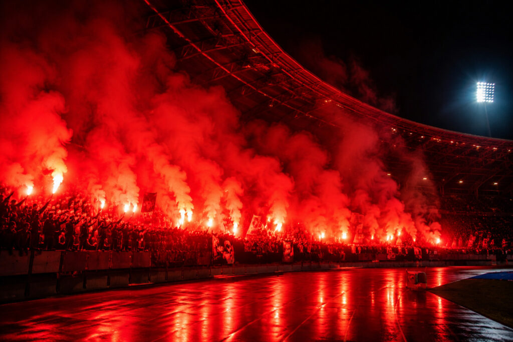 Czerwone flary stadionowe podczas nocnej oprawy kibicowskiej na dużym stadionie