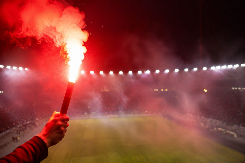 Odpalona czerwona flara stadionowa emitująca intensywne światło na tle stadionu nocą