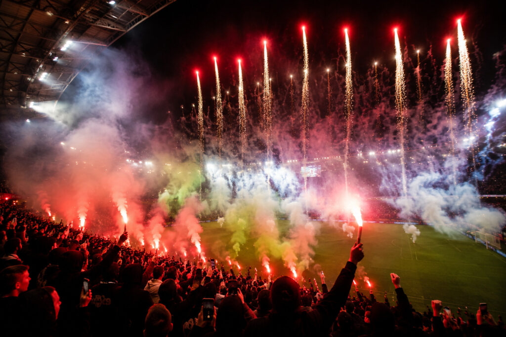 Oprawa stadionowa z flarami, świecami dymnymi i efektami pirotechnicznymi podczas nocnego pokazu