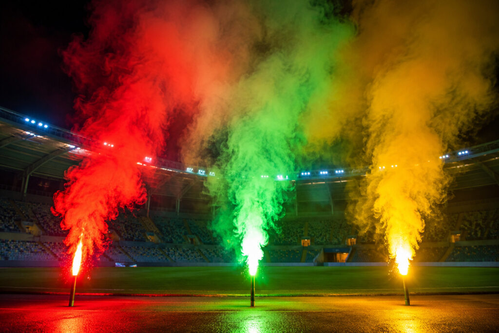 Kolorowe flary stadionowe emitujące czerwone zielone i żółte światło podczas oprawy na stadionie