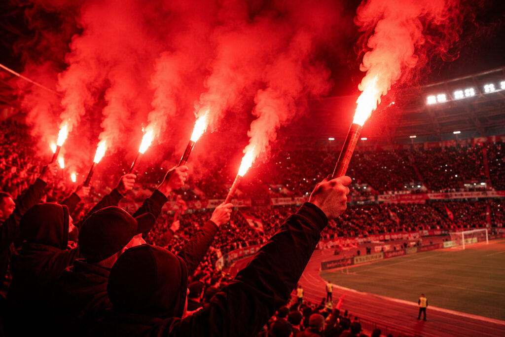 Kibice odpalający czerwone race stadionowe podczas oprawy meczowej