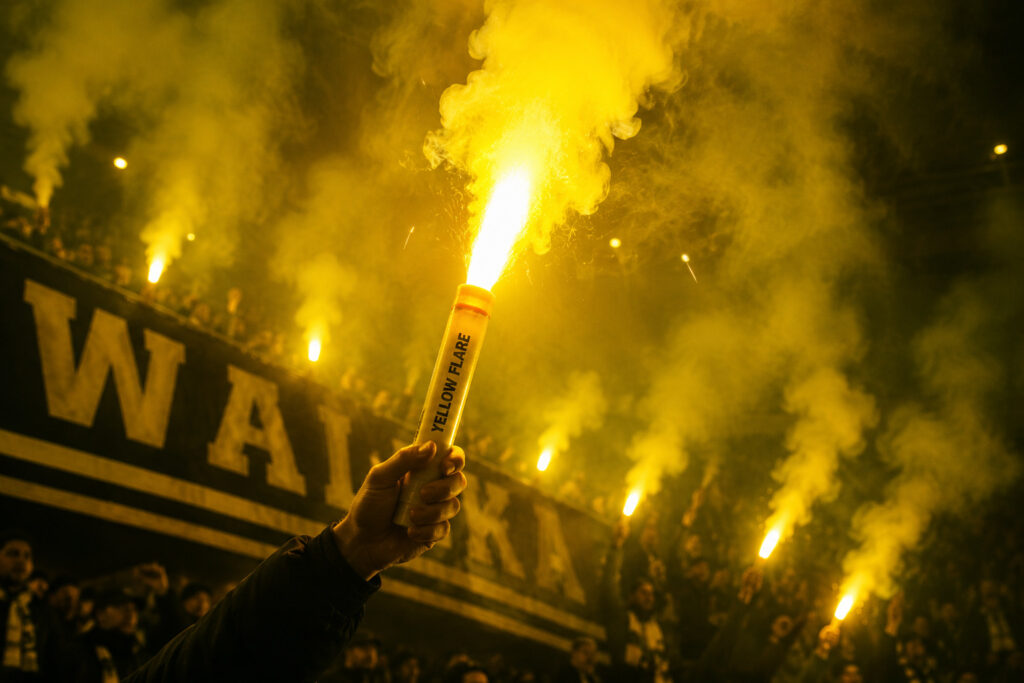 Żółta flara stadionowa emitująca intensywne żółte światło podczas oprawy kibicowskiej na trybunach