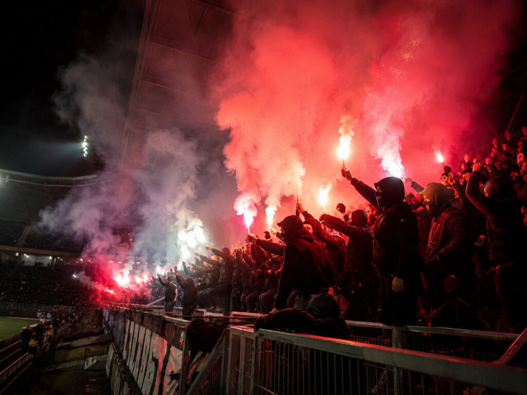 Kibice z czerwonymi i białymi racami stadionowymi na nocnej trybunie